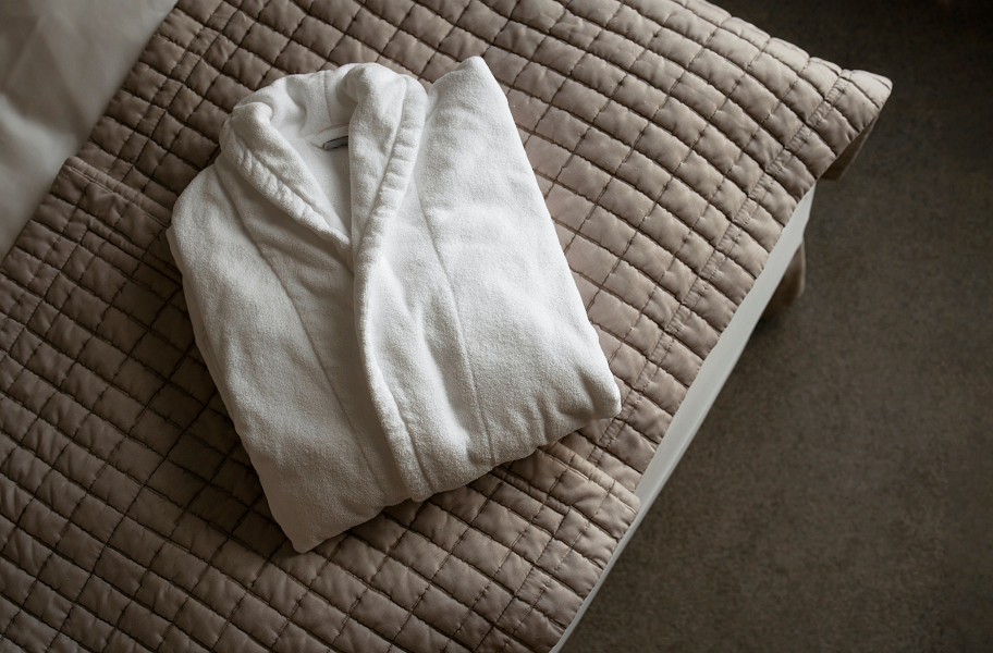 A folded white dressing gown on a bed.